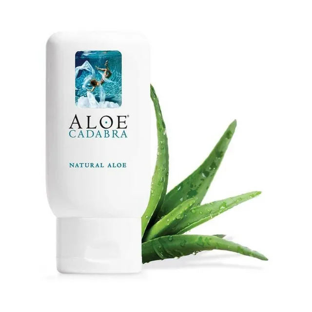 white Aloe Cadabra Natural Aloe lubricant bottle beside fresh aloe leaves