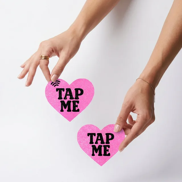 Neva Nude Tap Me pink glitter heart NFC pasties held between two hands with both hearts visible