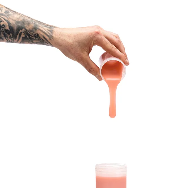 Hand pouring peach Clone-A-Willy silicone refill above open container