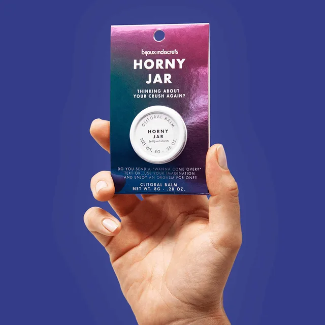 hand holding the packaged Horny Jar balm against a dark blue background