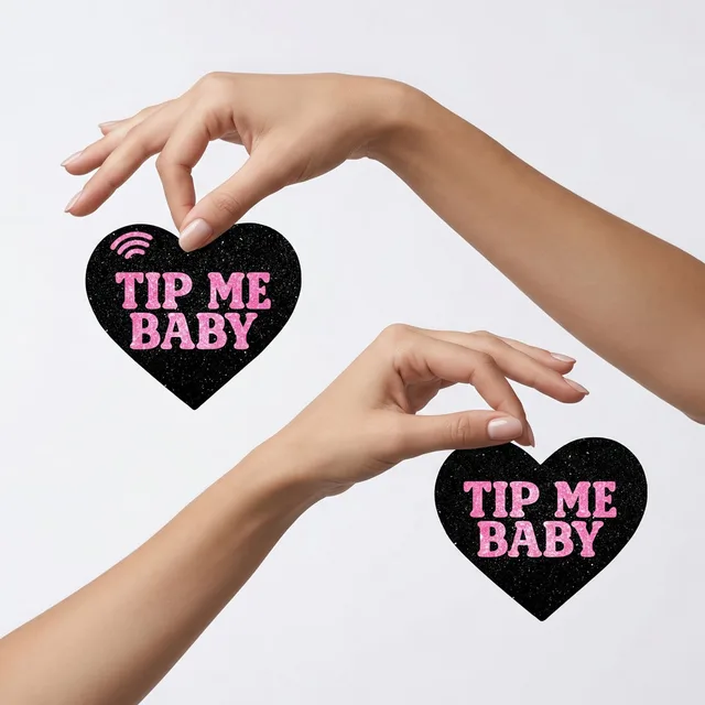 Neva Nude Tip Me Baby black heart NFC pasties held between two hands with the matching pair visible