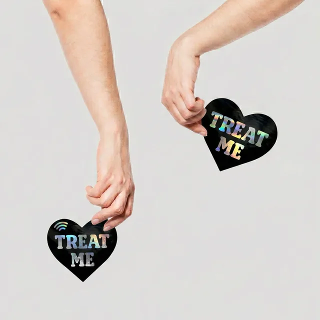 Neva Nude Holographic black holographic heart NFC pasties held between two hands with both hearts visible