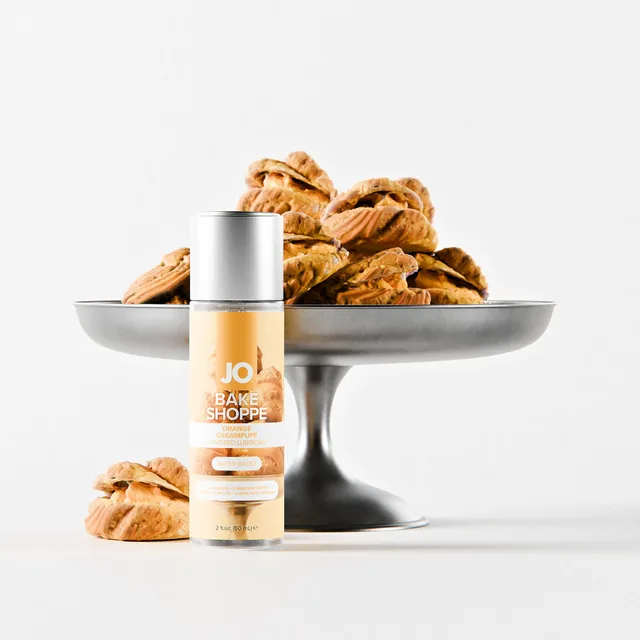 System JO orange creampuff water-based lube 2 oz bottle arranged beside orange cream puffs