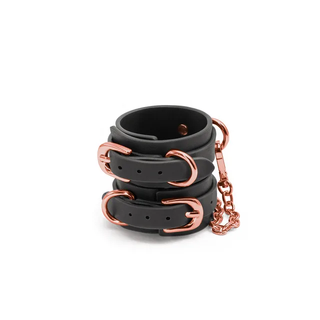 Stacked black wrist cuffs with rose-gold buckles and chain