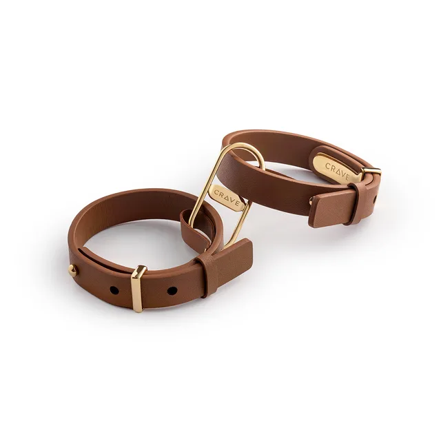 pair of tan leather Crave cuffs linked by polished gold D-rings
