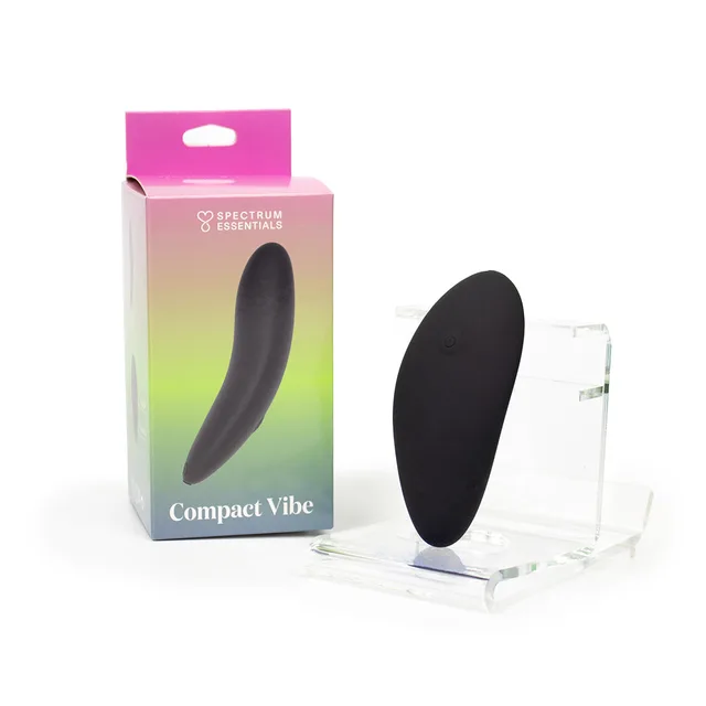 Spectrum Essentials black compact rechargeable external vibrator displayed beside its gradient retail box and clear stand