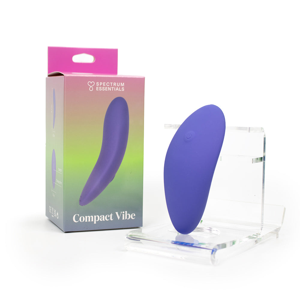 Spectrum Essentials Rechargeable Silicone Compact External Vibrator Purple Spectrum Essentials purple compact rechargeable external vibrator displayed beside its gradient retail box and clear stand
